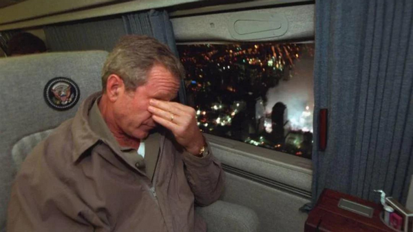 A white man wearing a brown coat holds his temples.
