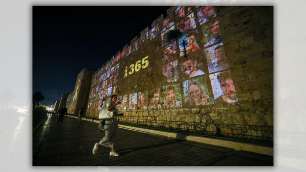 A person stands in front of a memorial that says 365 in yellow surrounding many images of people.